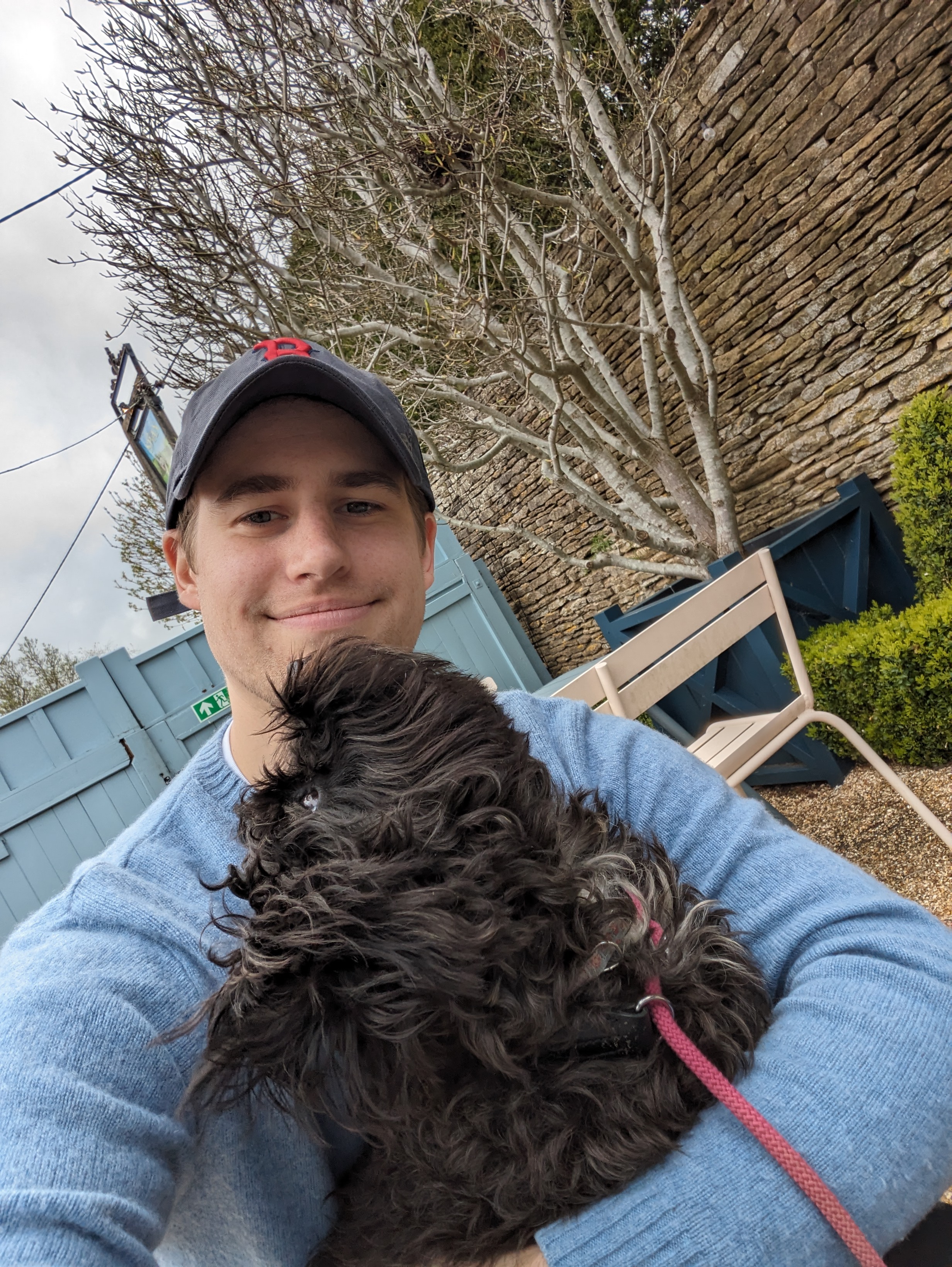 A picture of me in a baseball cap with a small black fluffy dog looking up at me
